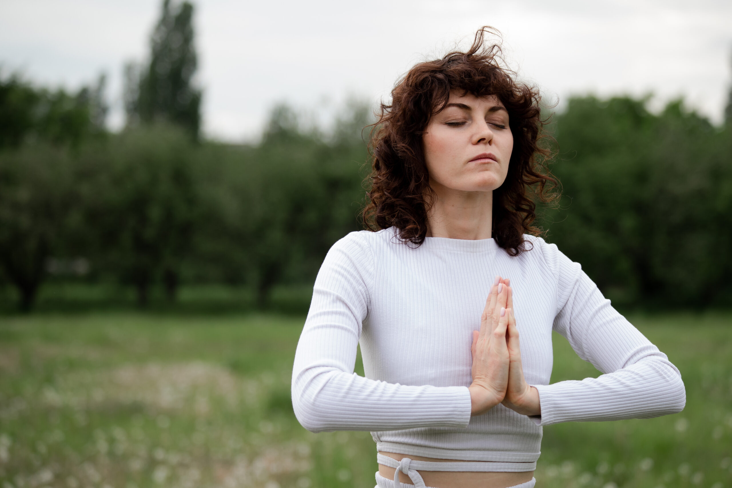 Full focus on meditation. Namaste sign. Adult woman in white sportswear folded palms together. Yoga position of young girl who closed eyes. Deep breathing technique. High quality photo